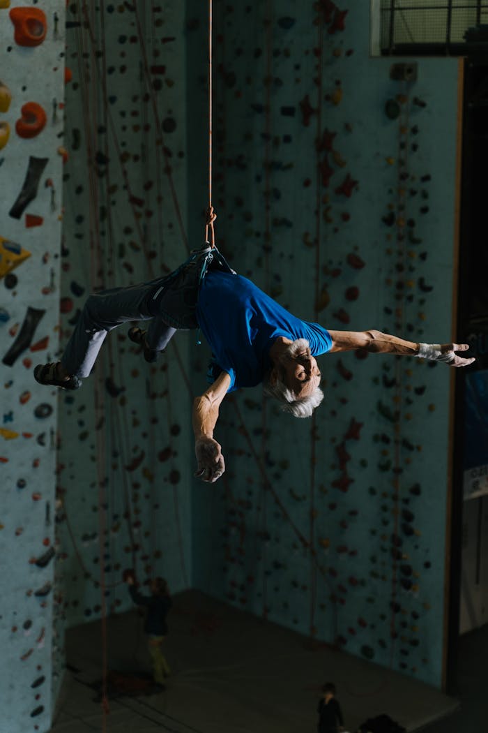 Senior man climbing in indoor facility on harness, displaying athleticism and balance.